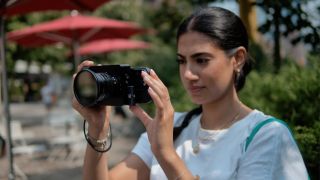 A person holds a mirrorless camera with a smartphone on the back