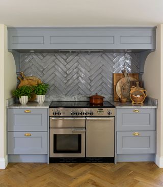 blue kitchen cabinets and steel range cooker with gray blue tiles in herringbone pattern and herringbone wooden floor
