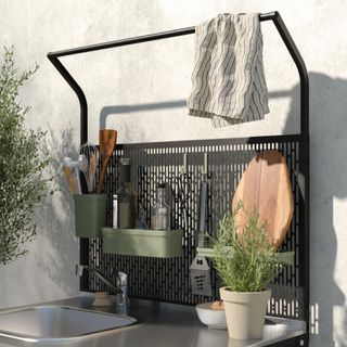 outdoor kitchen storage rack attached to outdoor sink, utensils and storage hanging from it, herb plant