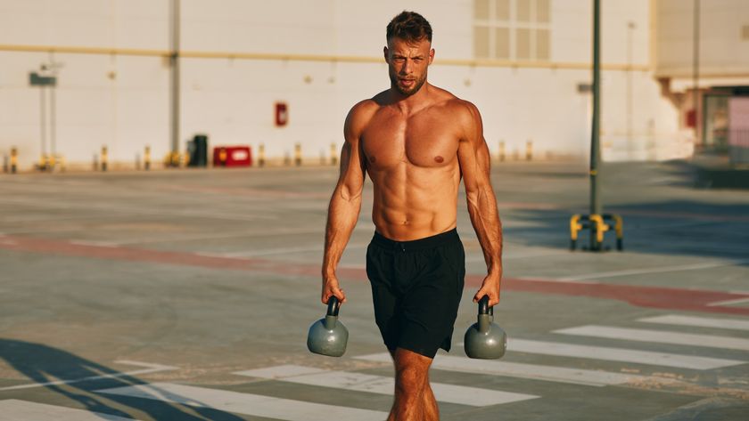 Muscular male walking with kettlebells outdoors