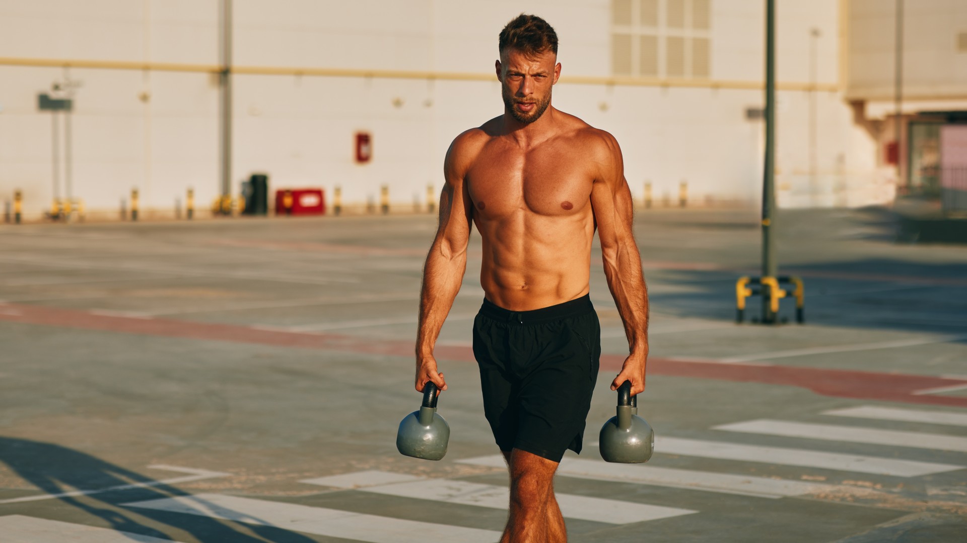 Muscular male walking with kettlebells outdoors