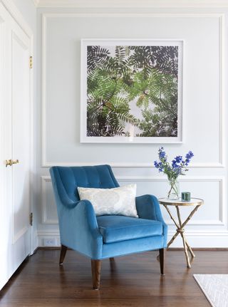 blue easy chair with paneled walls behind and leafy artwork in white frame
