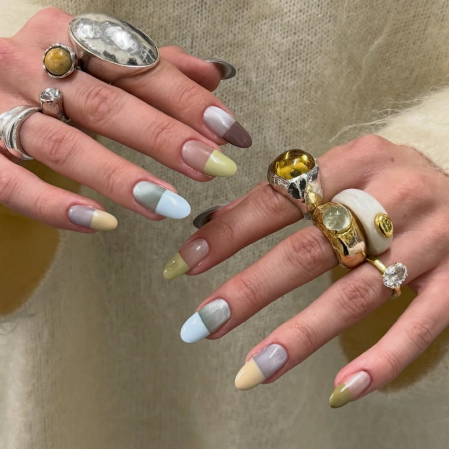 two hands with a ton of rings in both gold and silver with pastel, light nail polish colors