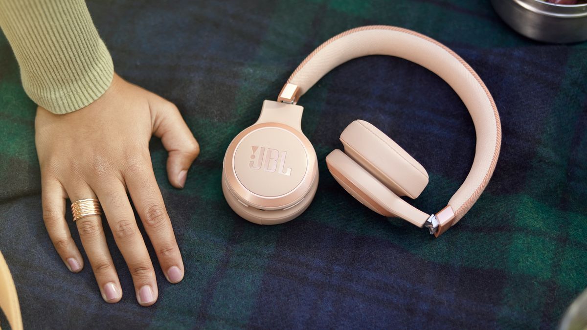 Woman&#039;s hand next to JBL Live 670NC headphones in rose.