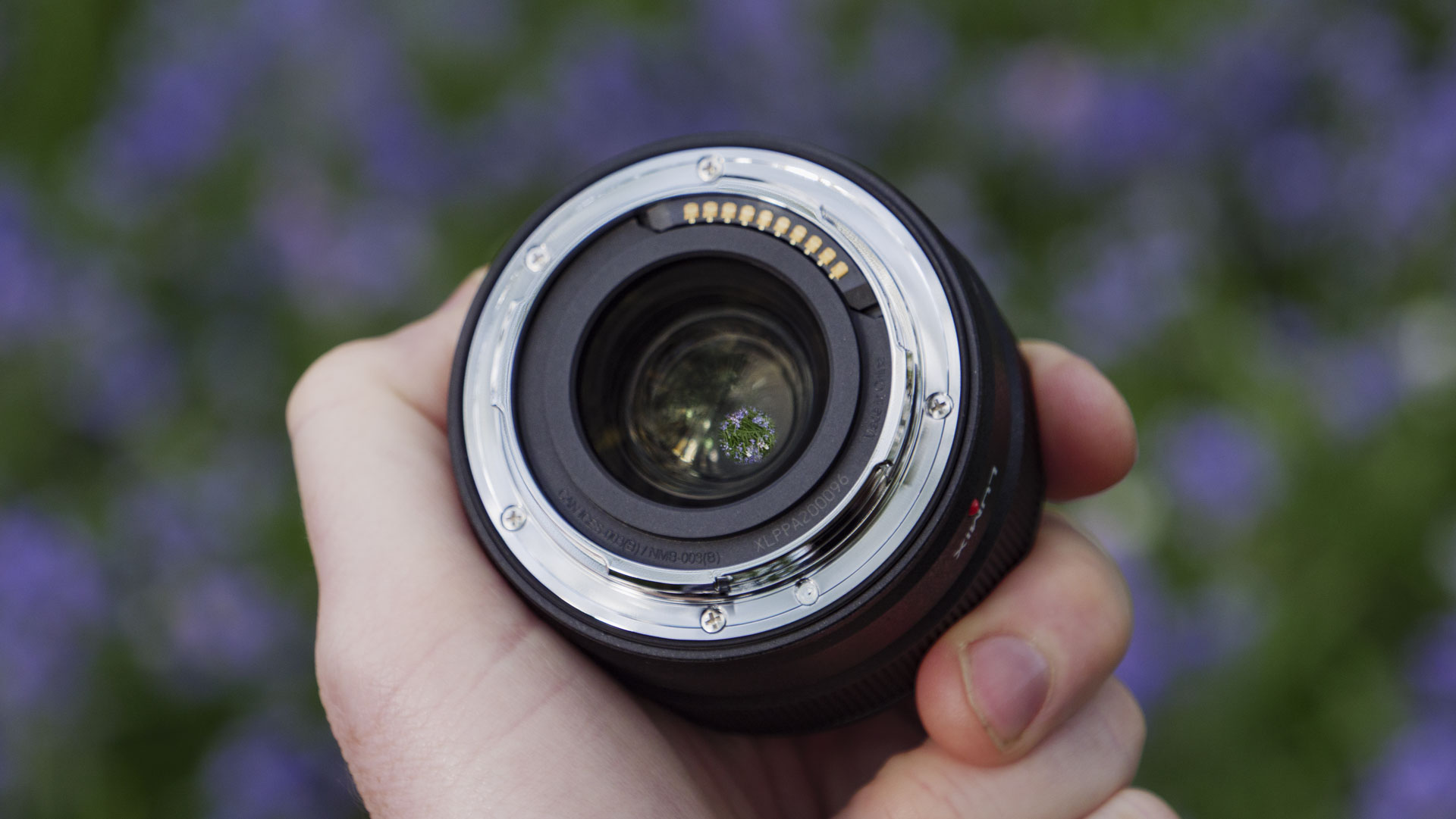 The rear mount of the Panasonic Lumix S 40mm F2 lens in the hand, with natural bluebell backdrop