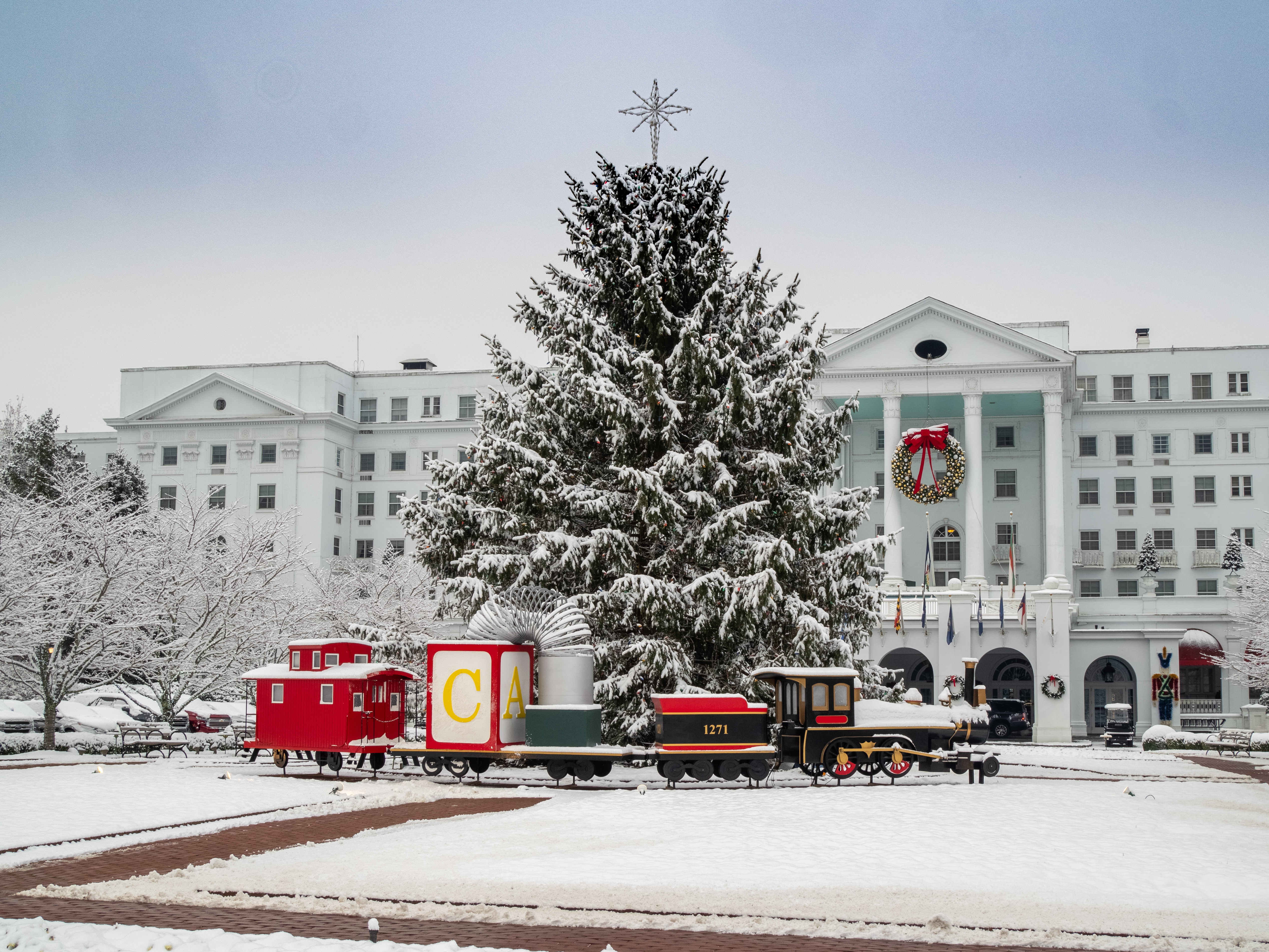 A large model train sits under a giant snow-covered tree in front of the Greenbrier Resort in West Virginia