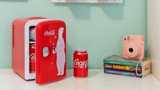 Koolatron KWCA4 mini fridge on desk next to book pile and pink Polaroid camera