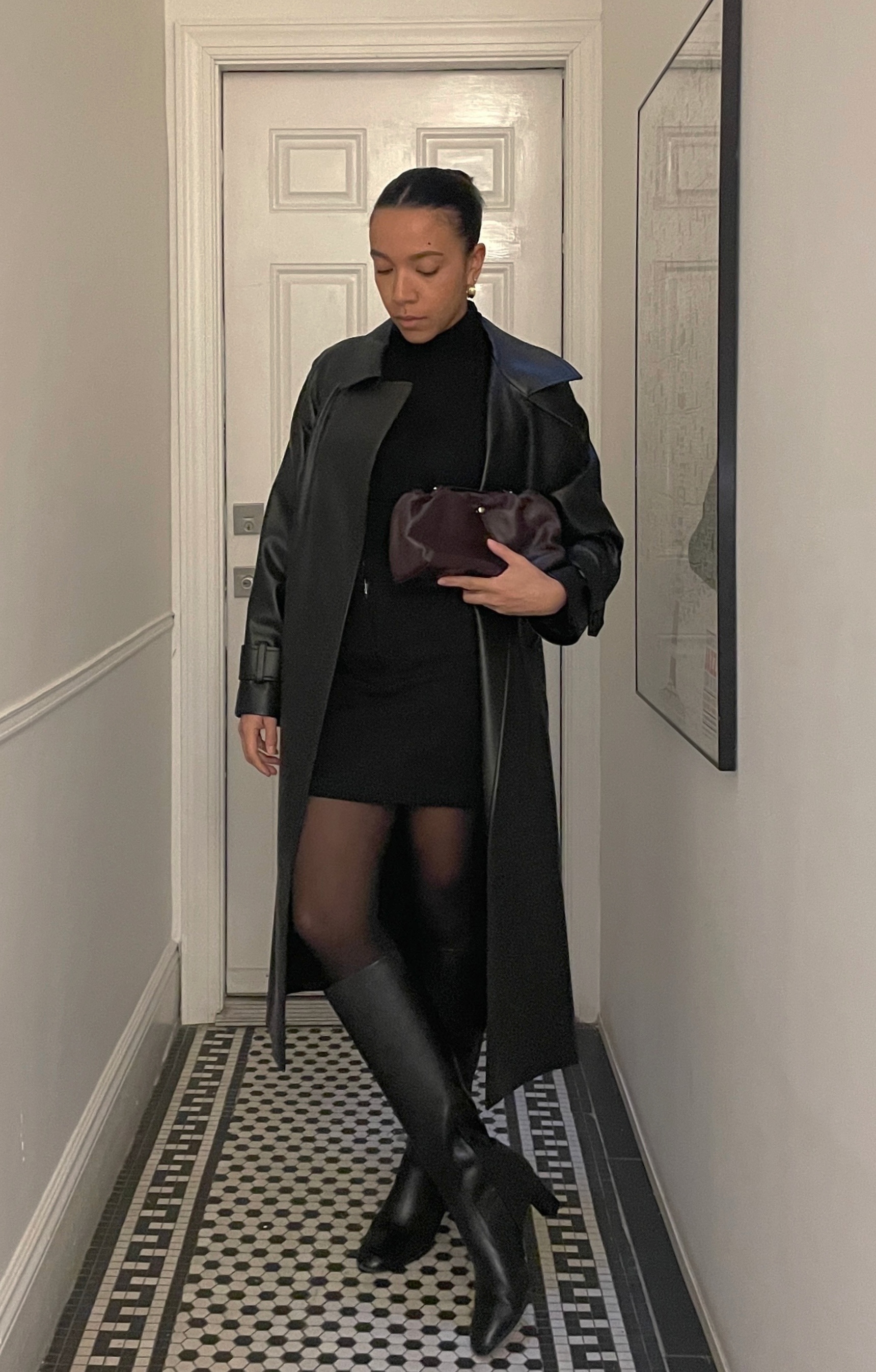 Lauren Tappan wearing a leather trench coat, a mini skirt, a turtleneck, sheer tights, and black boots