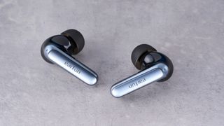 a pair of silver and black shiny earbuds with a black matte charging case are photographed against the Tom's Guide blue background