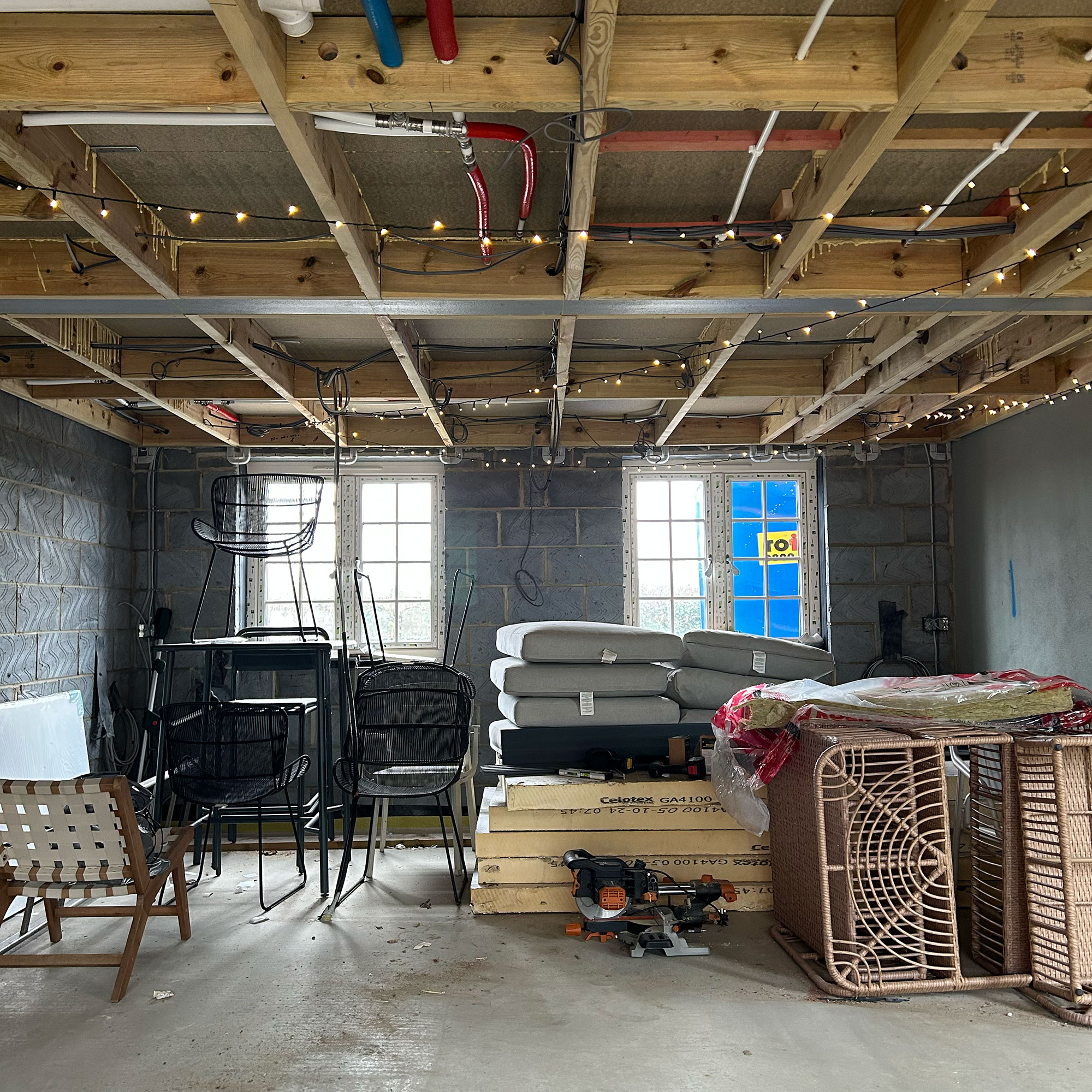 Room mid-renovation with piles of furniture on concrete flooring and fairy lights strung from exposed ceiling