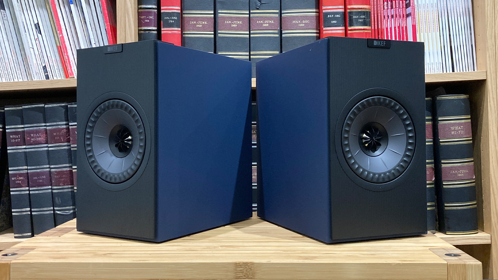 KEF Coda W active speakers on wooden hi-fi rack in front of bookcase
