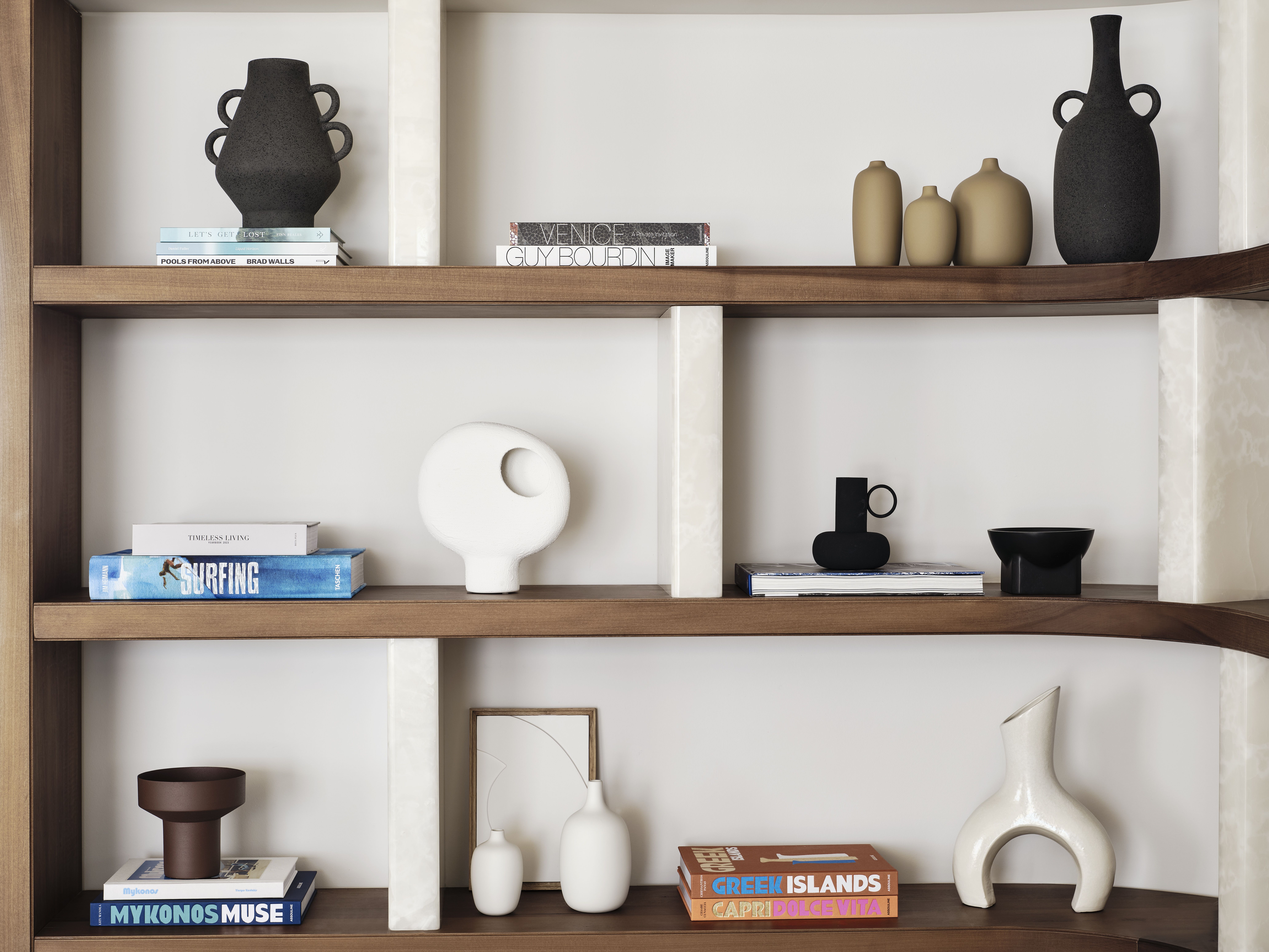 A beautifully curated, contemporary wooden shelf filled with sculptural collectibles like ceramic vases and candleholders, books, and more.
