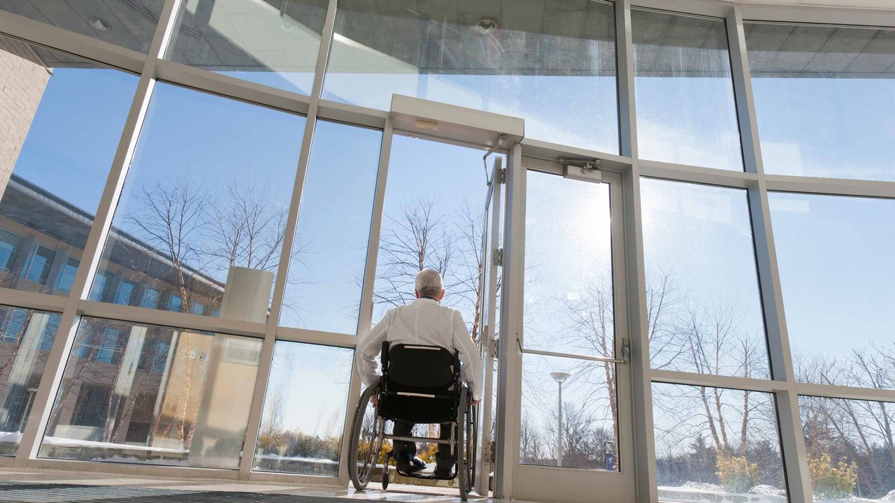 A man in a wheelchair attempt to enter an office building.