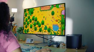 Person at desk with pink t shirt and curly hair playing Stardew Valley on Steam Machine with mouse and keyboard.