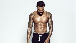 Tattooed physical athlete in front of light background