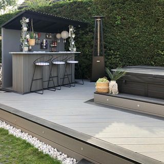 Grey composite decking with outdoor bar and stools next to ivy wall