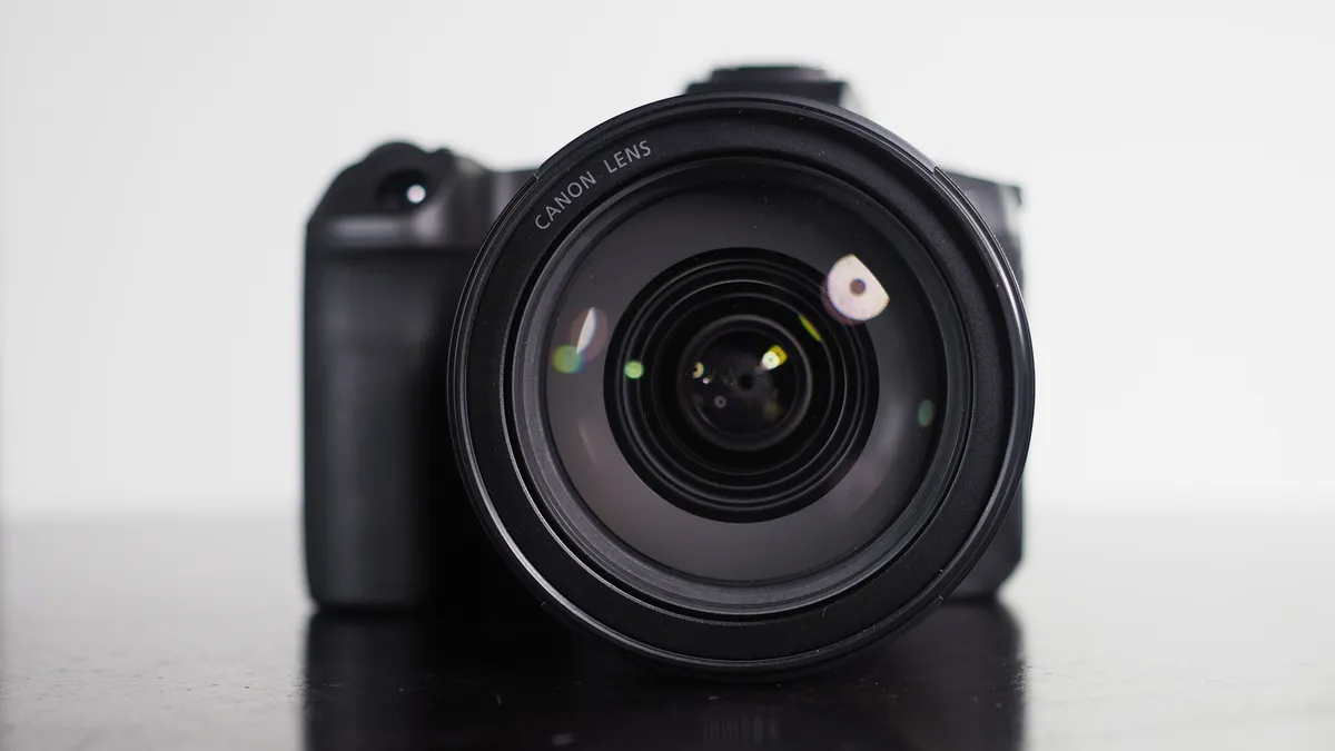 Close-up of a Canon camera lens, showcasing its glass and black body, resting on a dark surface against a plain white background