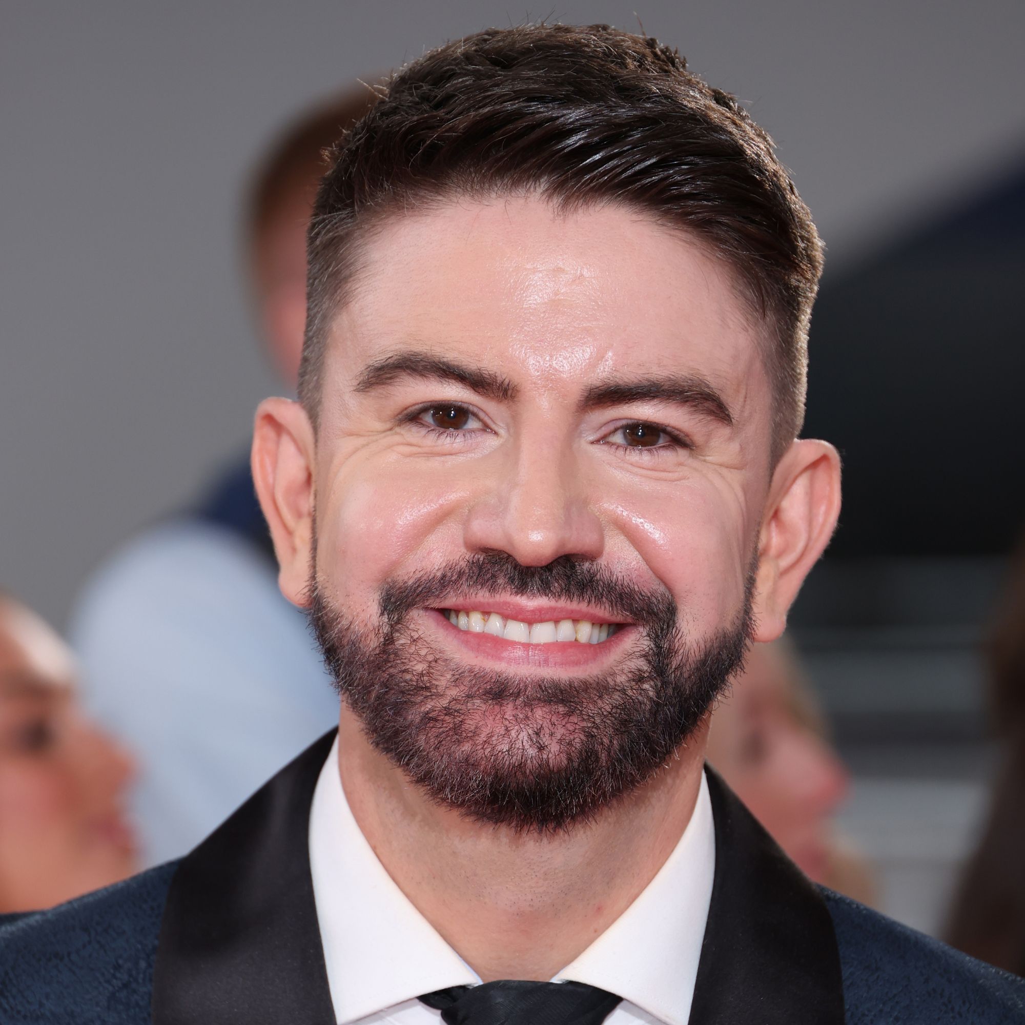 Headshot of Iwan Carrington wearing a suit, smiling in front of the camera on a red carpet
