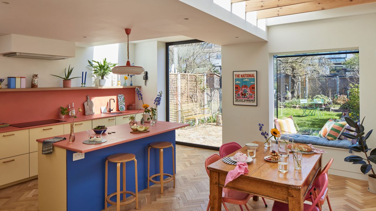 Colourful kitchen with blue island, pink work surfaces and wooden table with pink metal chairs