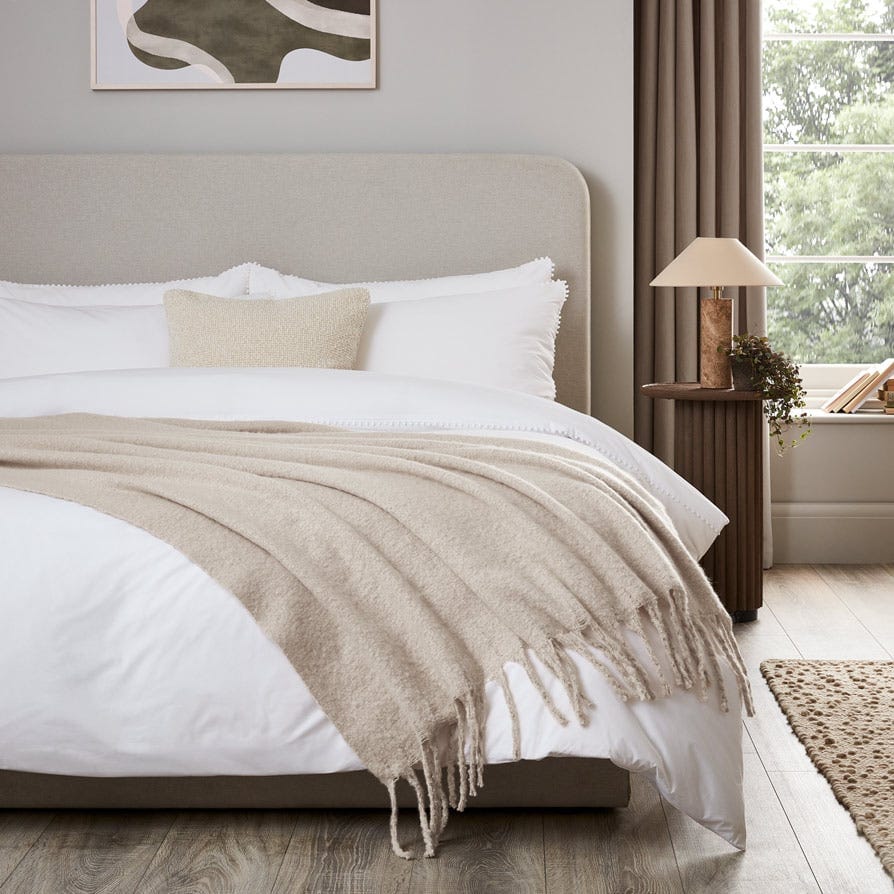 A bed with white bedding and a mohair throw drpaed across it