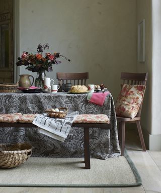 Fall table decor ideas with a grey patterned tablecloth, orange and pink seat cushions and orange and pink flowers