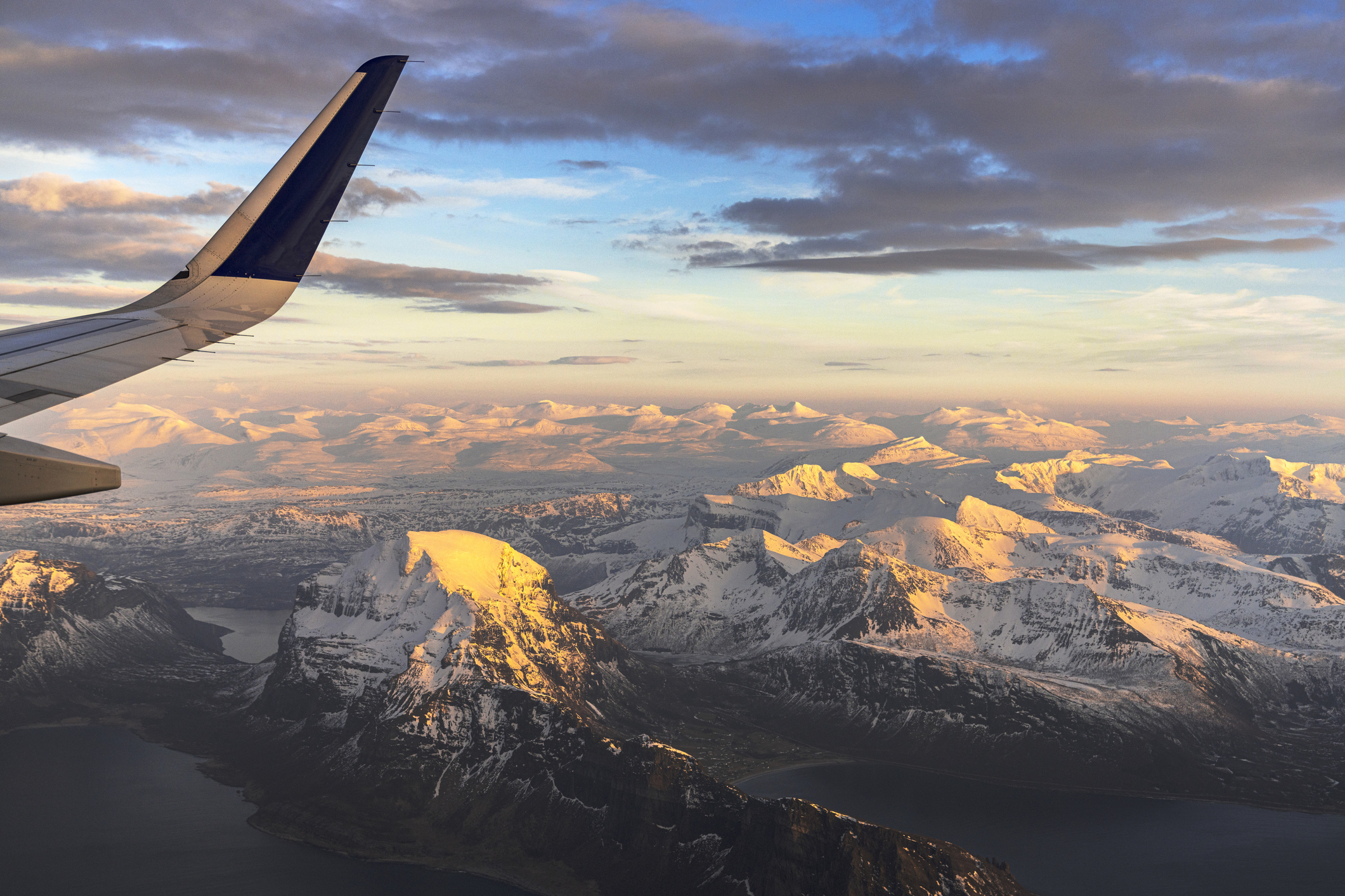 Airplane in flight over snowcapped mountains and frozen sea at sunset, Bodo , Nordland county, Lofoten Islands, Norway.