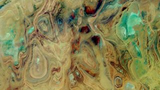 A satellite photo of the Sahara showing colorful rock folds and salt flats that look like abstract art 