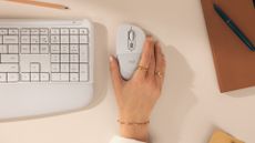 The Logitech Signature Comfort Plus keyboard and mouse pictured on a desk with woman's hand holding mouse.