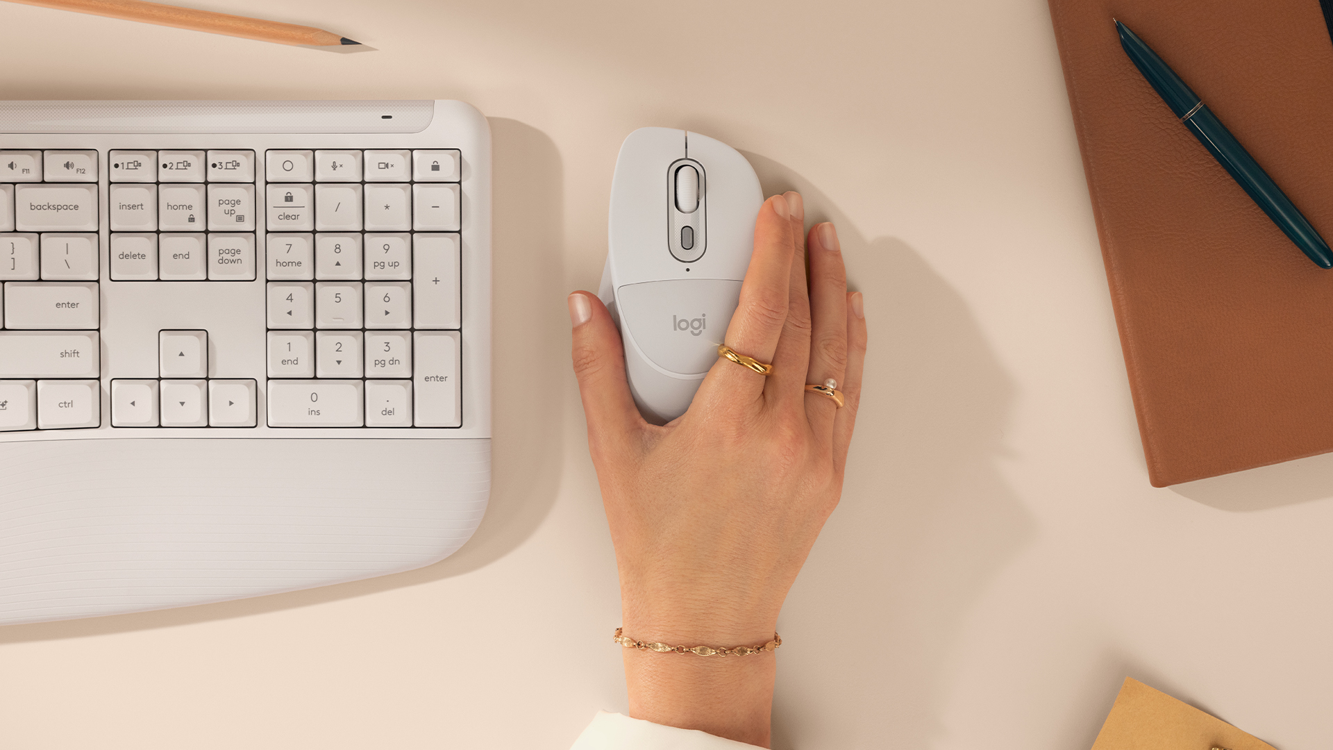 The Logitech Signature Comfort Plus keyboard and mouse pictured on a desk with woman's hand holding mouse.