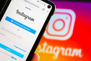 The Instagram login screen shown on a smartphone held in front of the Instagram logo