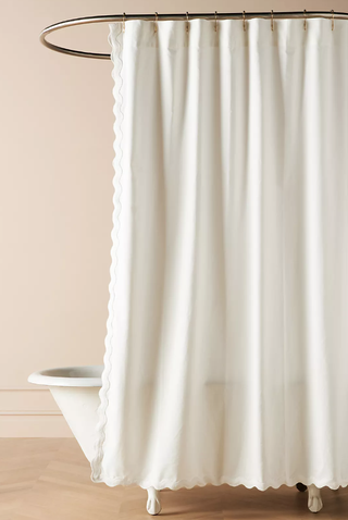 ivory shower curtain with scalloped edges hangs over a clawfoot bath tub