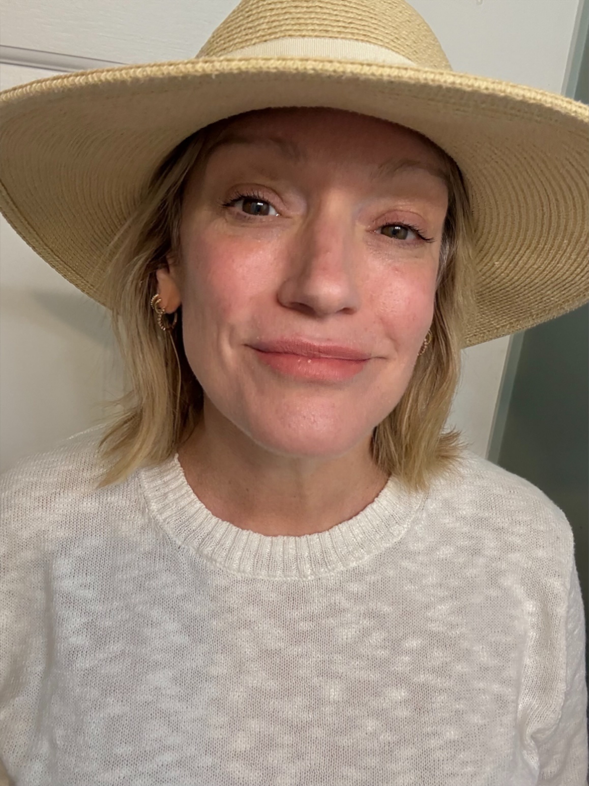 a woman with a tan sun hat and a white sweater after applying spf.