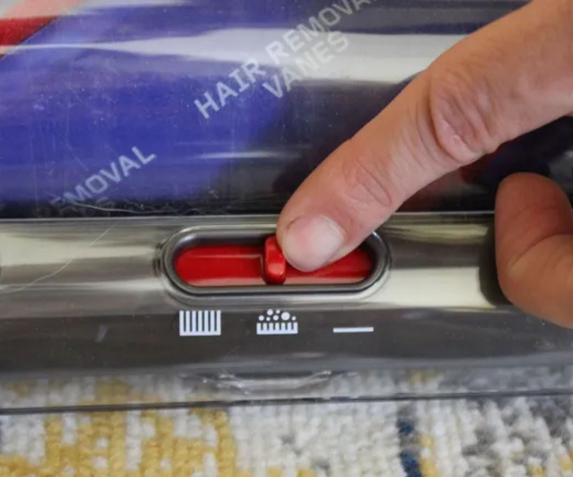 Closeup of the power adjuster slider on the floorhead of the Dyson Ball Animal 3 upright vacuum, on patterned rug in Camryn Rabideau's home