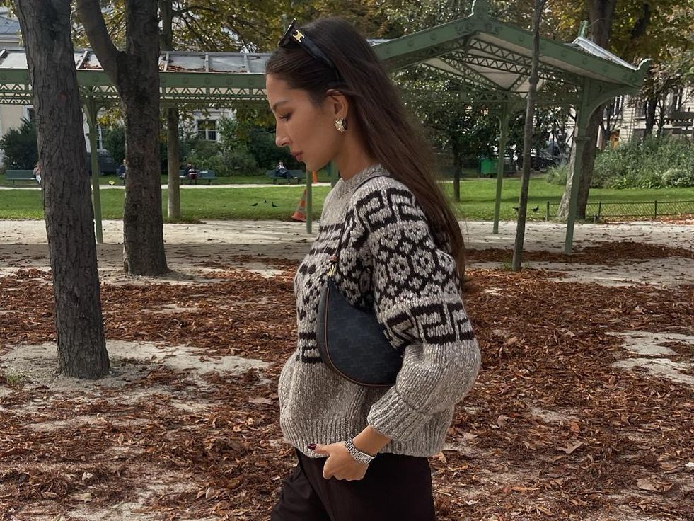 Woman wearing a perfect fall outfit with chunky knitwear, black jeans and gold accessories.