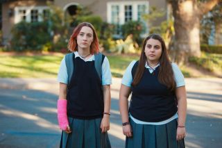 saoirse ronan with a cast on and beanie feldstein in school uniforms standing on a street in lady bird