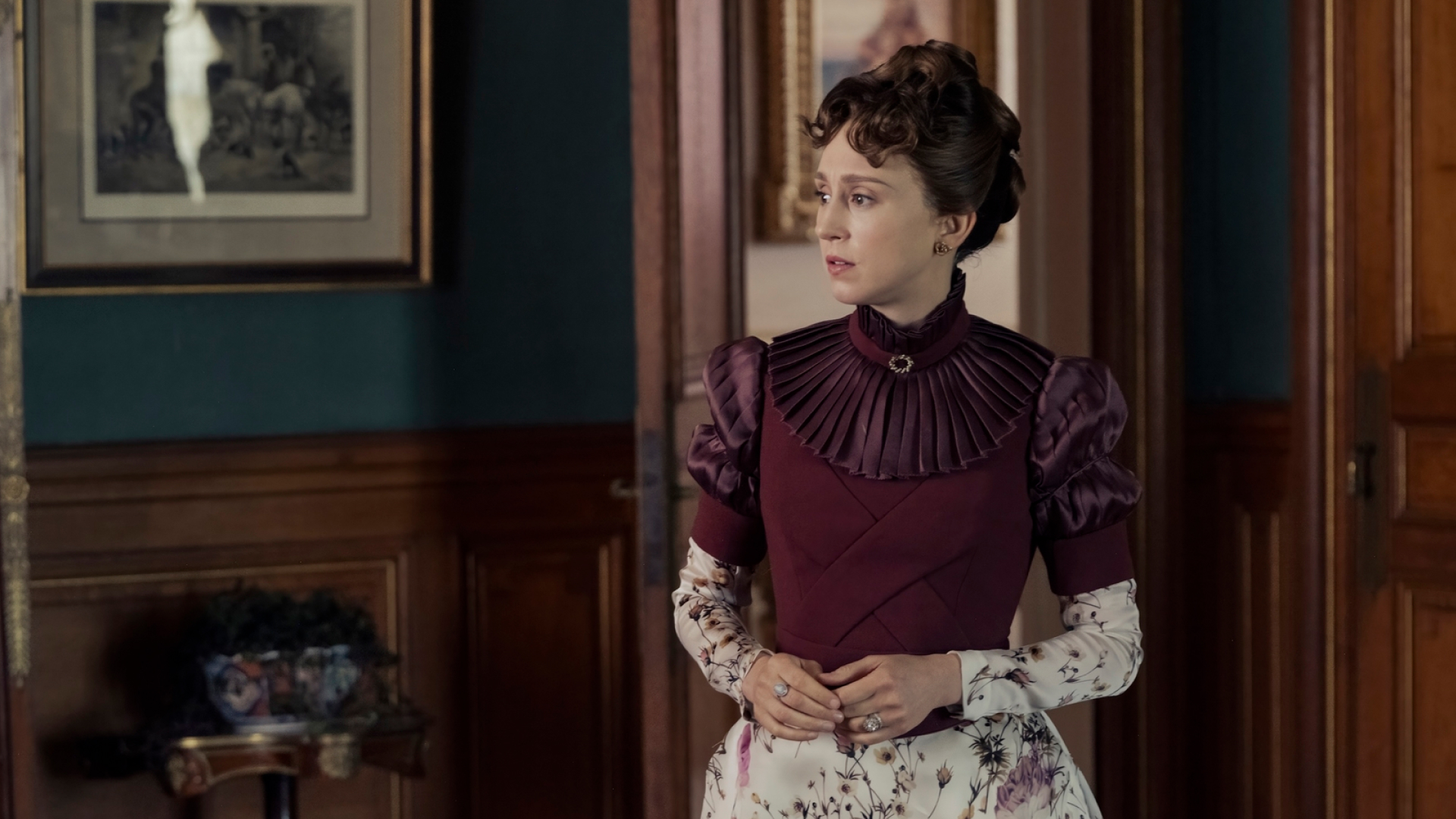 taissa farmiga as gladys russell wearing a maroon and floral dress standing in a parlor in the gilded age