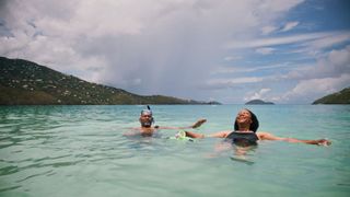 Woman and man floating in ocean wearing snorkel goggles