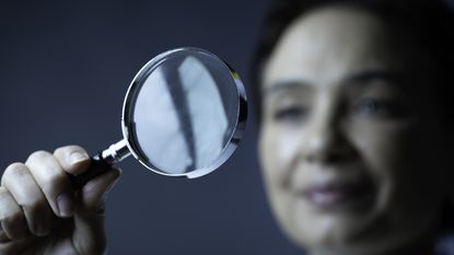 A woman holds up a magnifying glass.