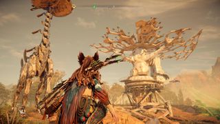 Aloy stands underneath a Tallneck next to a broken-down satellite
