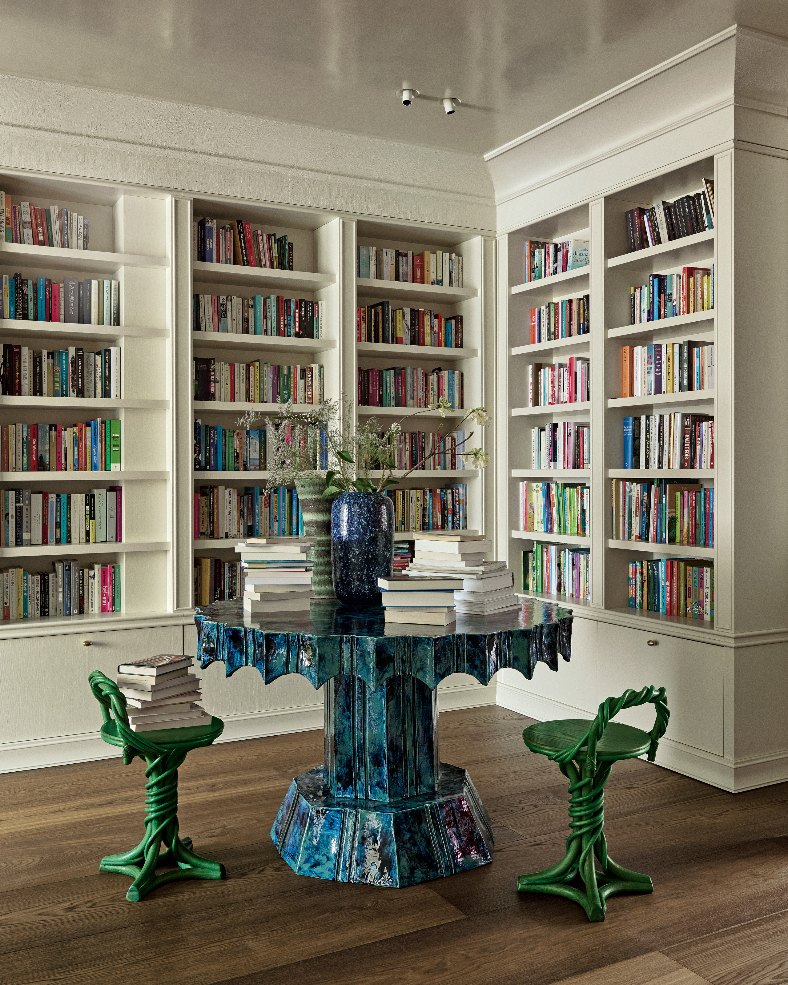 Library with built-in white bookshelves, blue sculptural library table and green stools