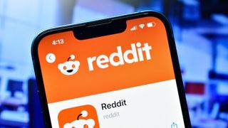 Reddit app logo on a phone with blue screens in background