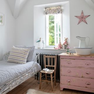 sunny, white-painted children's room with wrought iron bed, vintage pink chest of drawers and vintage ornaments