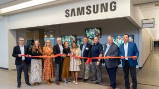 A group of Samsung executive smile with big scissors as they cut the ribbon on a new location.