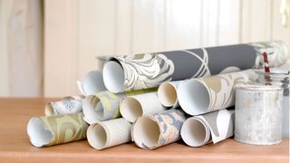 Rolls of wallpaper, jars and paint brushes on wooden table