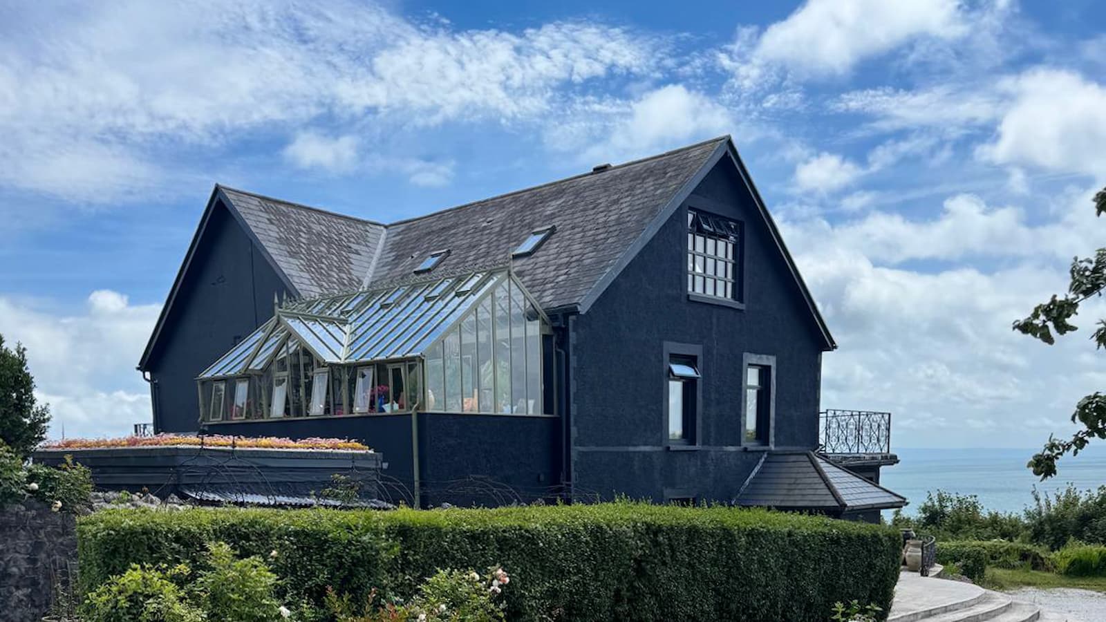 A dark blue house with a greenhouse attached to the side and a balcony