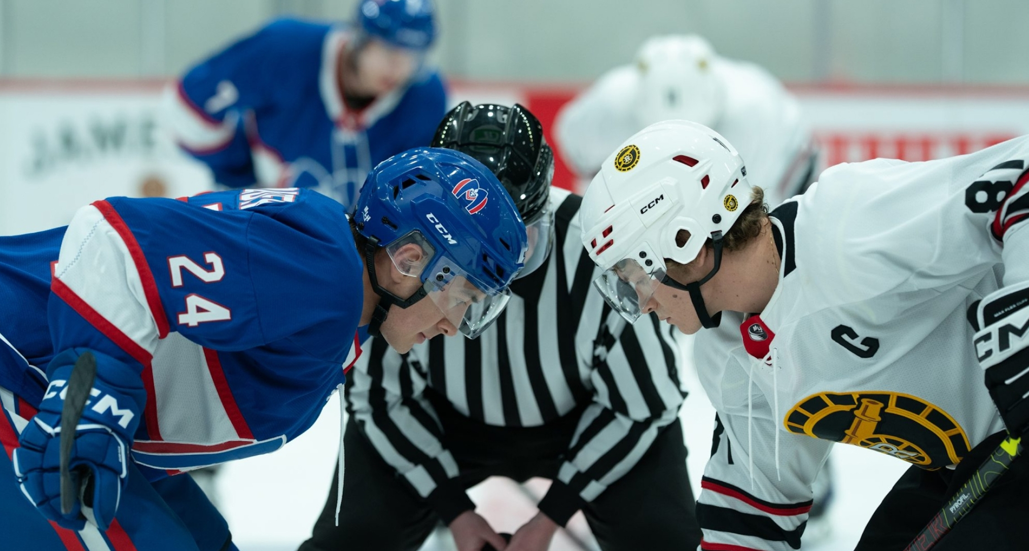 heated rivalry still of hudson williams as shane and connor storrie as ilya in their hockey gear on the ice ready to face off by a referee 