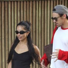 Zoe Kravitz wearing black sunglasses, a black tank top, blue shorts, and black flats