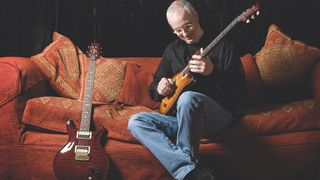 Paul Reed Smith playing one of his builds while seated on a couch