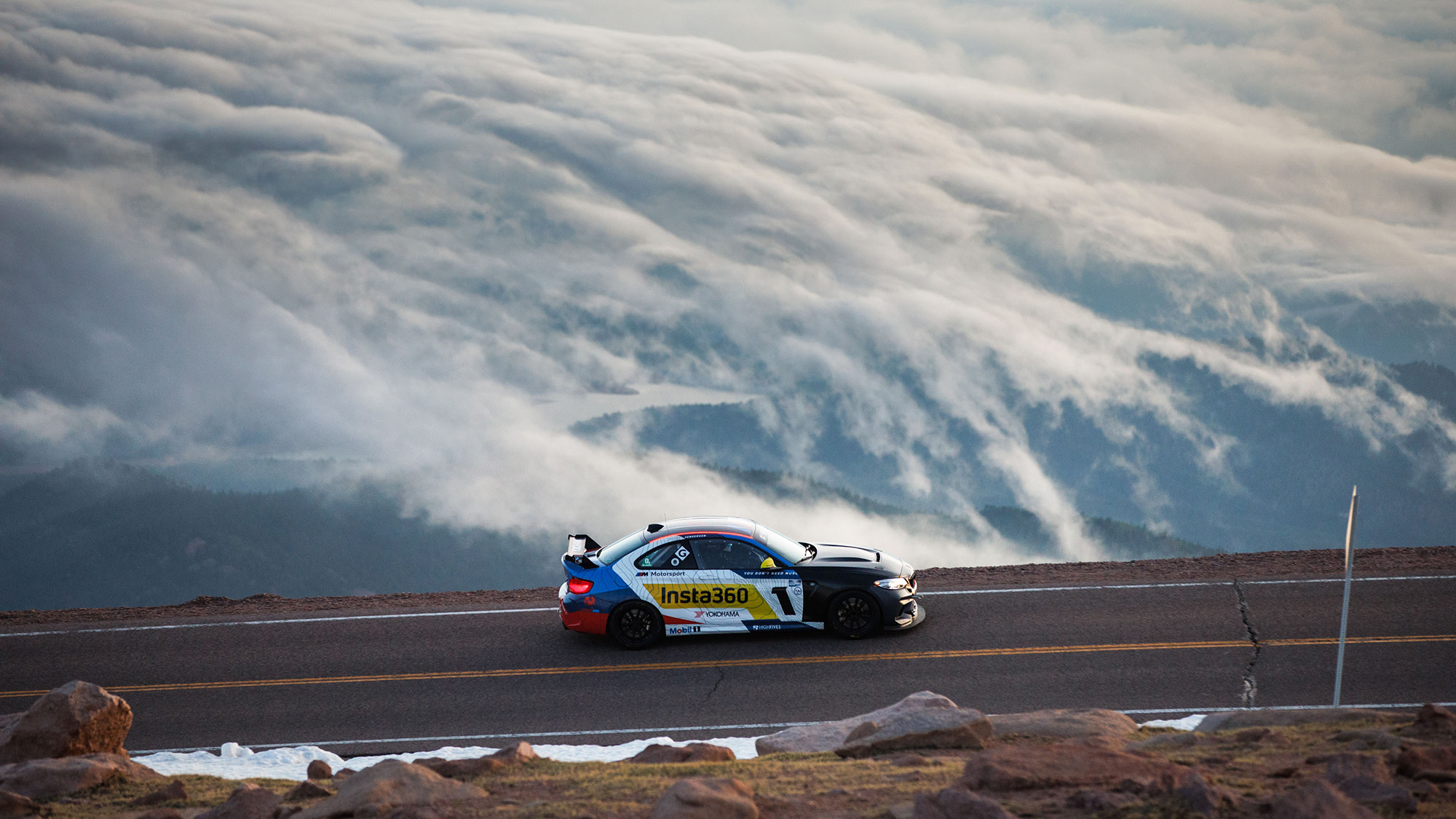 BMW car races up Pikes Peak against a backdrop of clouds 