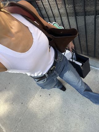 Eliza Huber wearing a white tank top, blue jeans, and a black belt